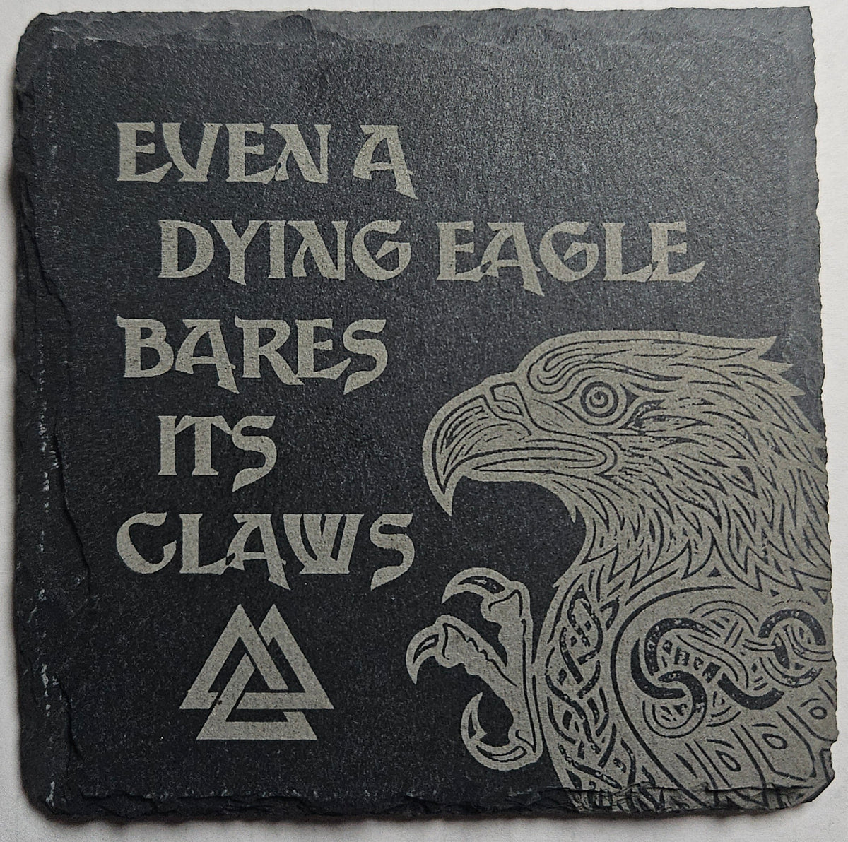 Decorative stone with engraved eagle and text that reads "Even a Dying Eagle Bares its Claws" on a gray background