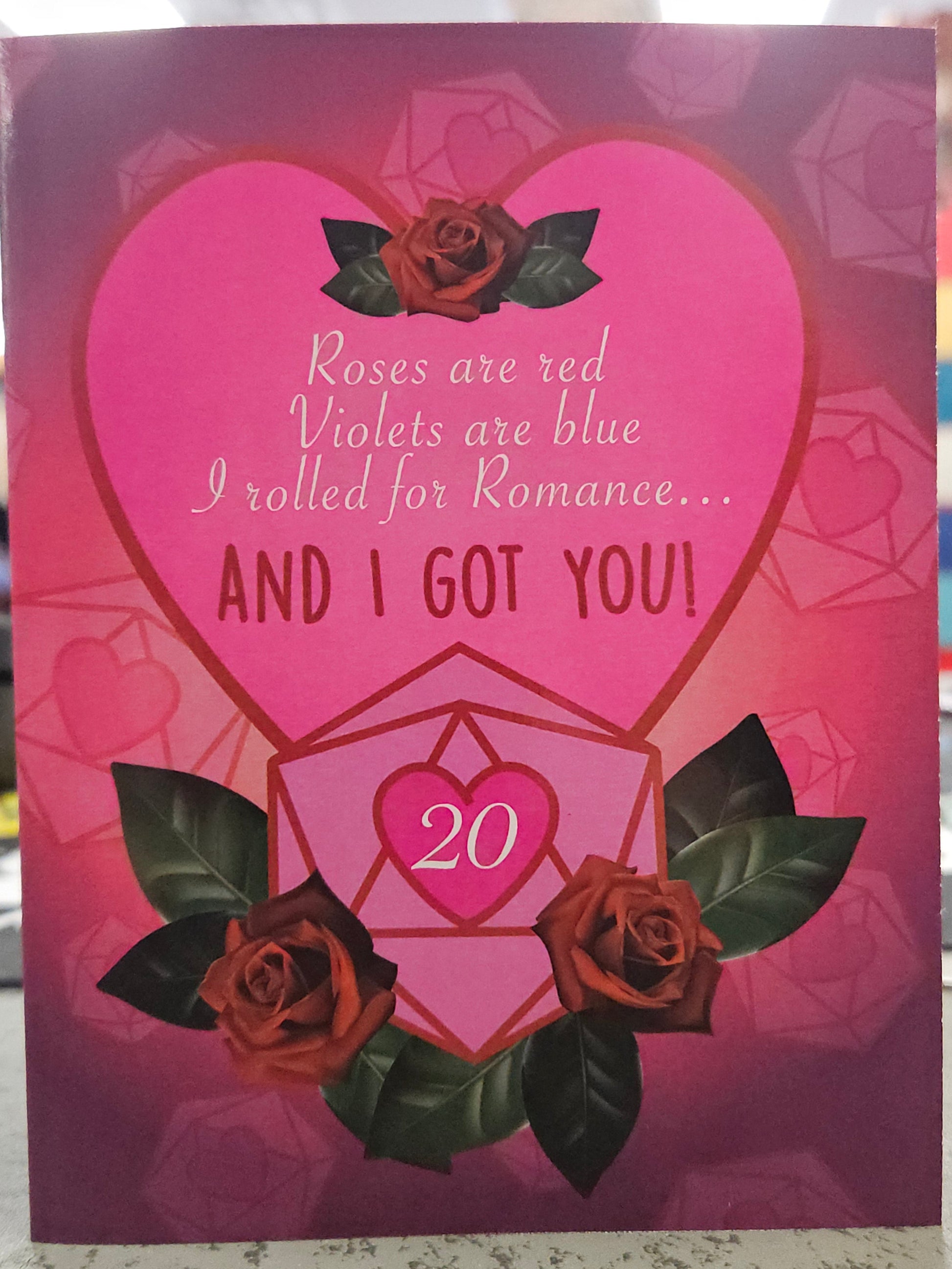 Valentine's Day card with pink heart and rose design on a blurred background with text that reads, "Roses are red, Violets are blue, I rolled for Romance... And I Got You!" featuring a pink D20 wit2 a Hot pink heart and the number 20 inside